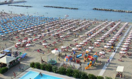 Überfüllter Strand mit Sonnenschirmen und einem Pool in der Nähe des Meeres.