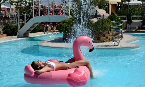 Person auf Flamingo-Schwimmreifen im Pool mit Wasserspritzern.